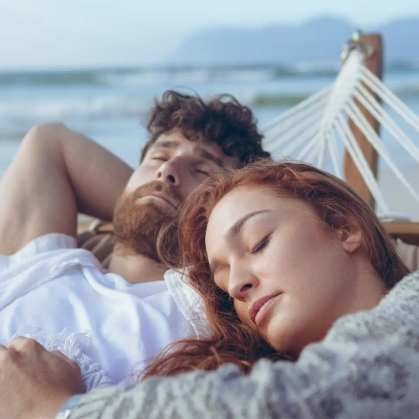 A man and a woman having a restful moment while laying on a hammock.